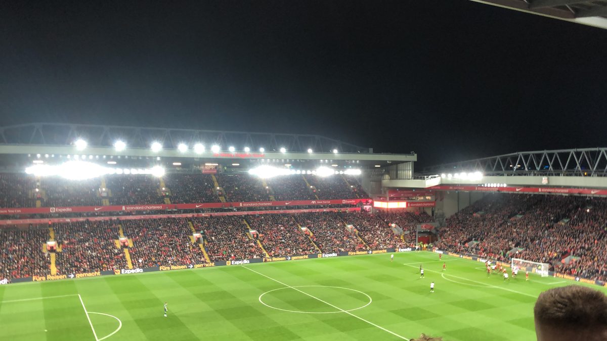 Anfield under floodlights at night, with a full crowd in the Sir Kenny Dalglish Stand
