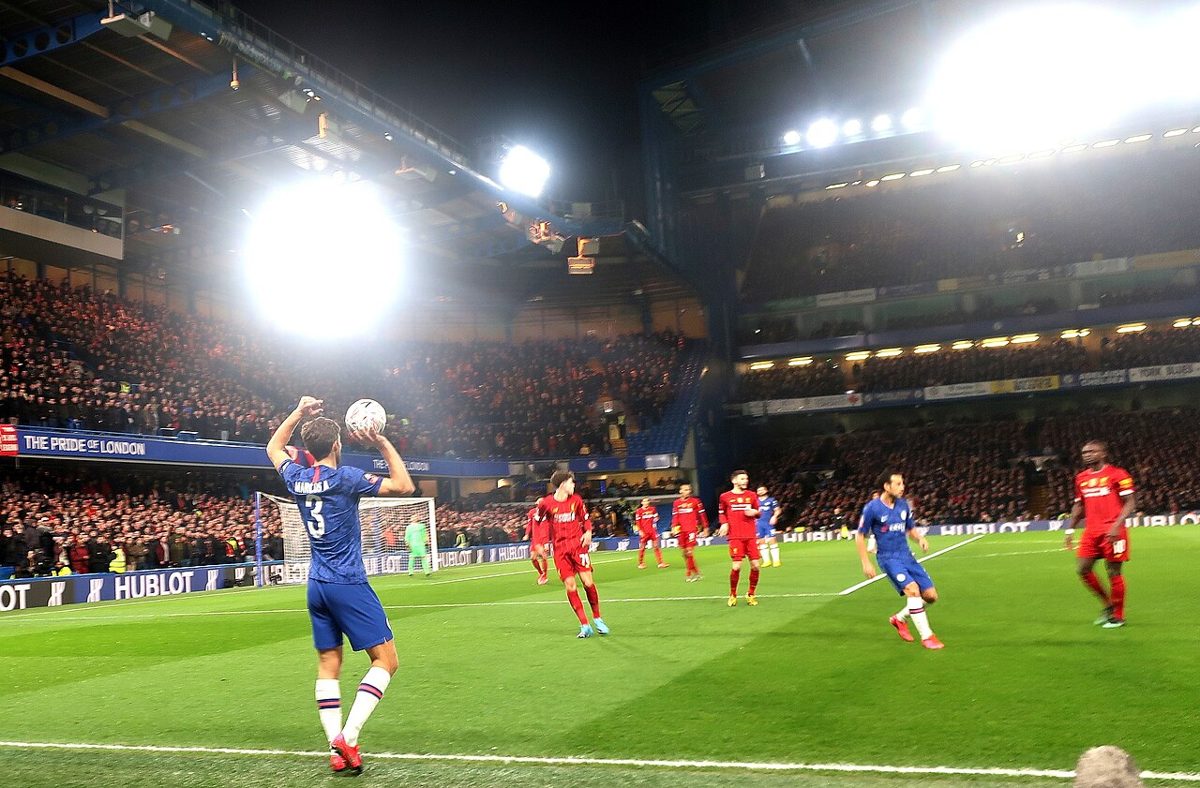A night match under floodlights, with a Chelsea player taking a throw-in against Liverpool